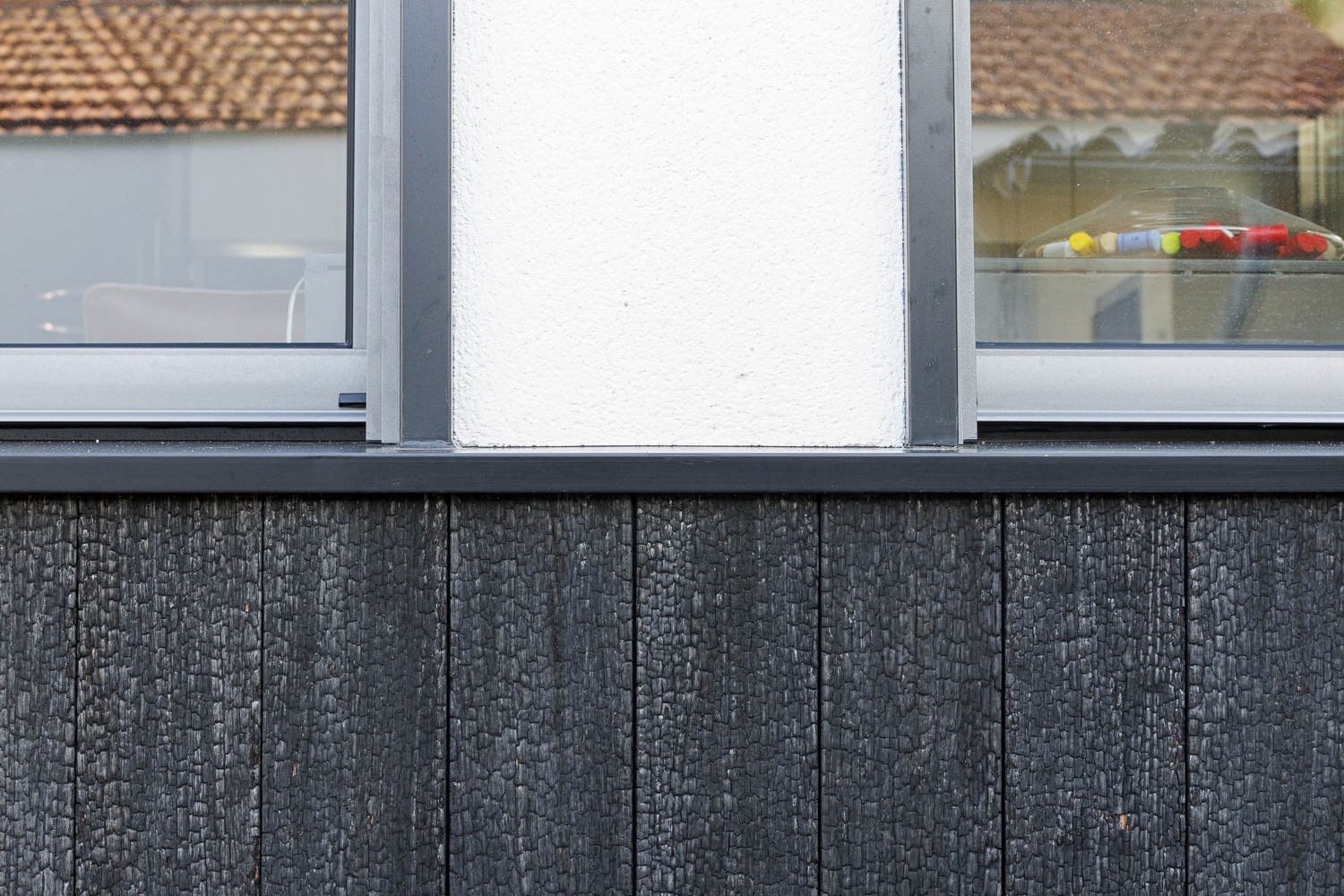 Bardage en bois brûlé noir texturé sous une façade blanche et des fenêtres modernes grises reflétant un toit de tuiles.