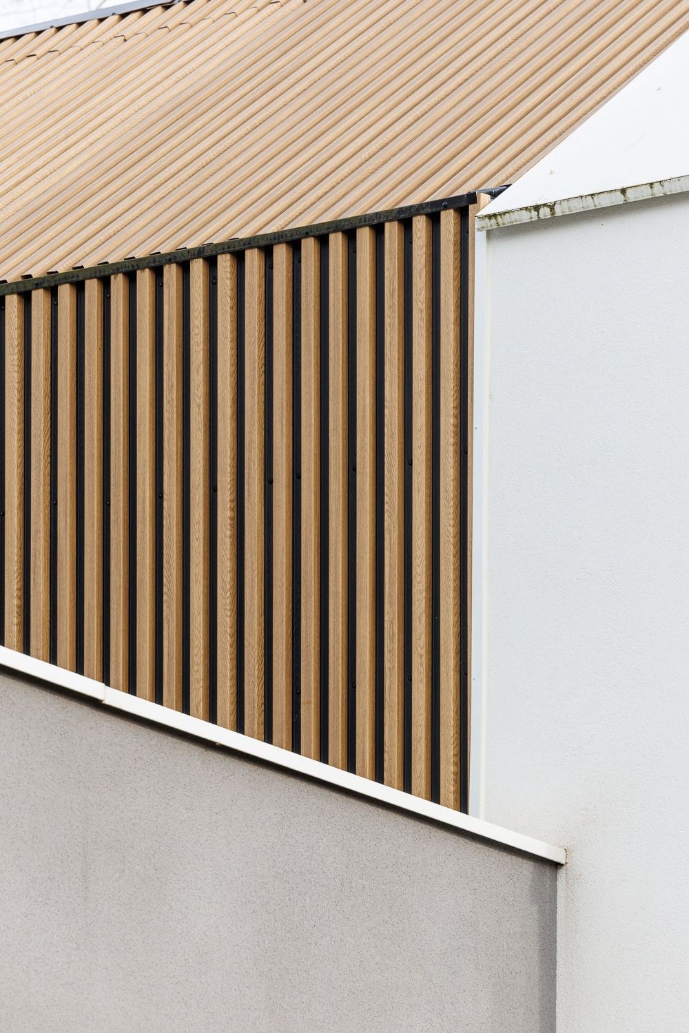 Bardage bois vertical et toit ondulé brun sur une façade d'architecture moderne aux murs gris et blanc.