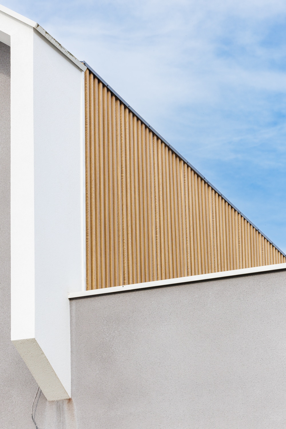 Façade de bâtiment moderne avec bardage bois vertical, mur gris et blanc sous un ciel bleu dégagé.