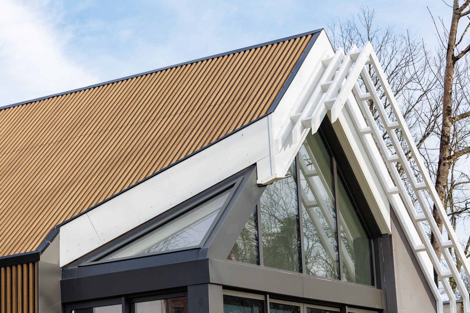 Détail d'un toit moderne ondulé avec charpente blanche apparente et grandes fenêtres triangulaires vitrées.