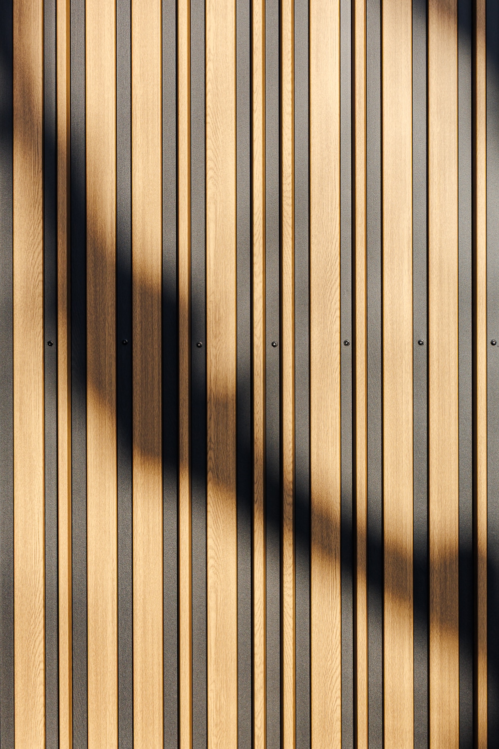Bardage vertical en bois clair et métal noir avec une ombre portée diagonale stylisée.