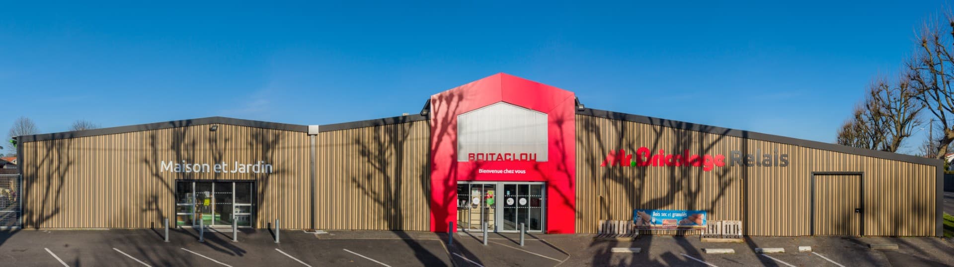 Façade du Boitaglou Mr. Bricolage Relais avec enseigne Maison et Jardin. Extérieur moderne sous un ciel bleu radieux.