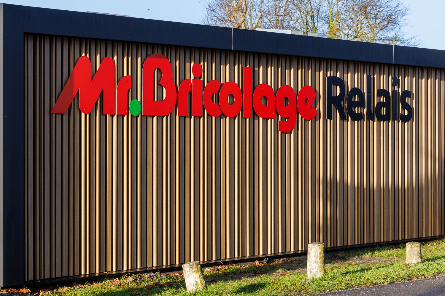Enseigne Mr. Bricolage Relais en lettres rouges et noires sur une façade en bois à claire-voie.