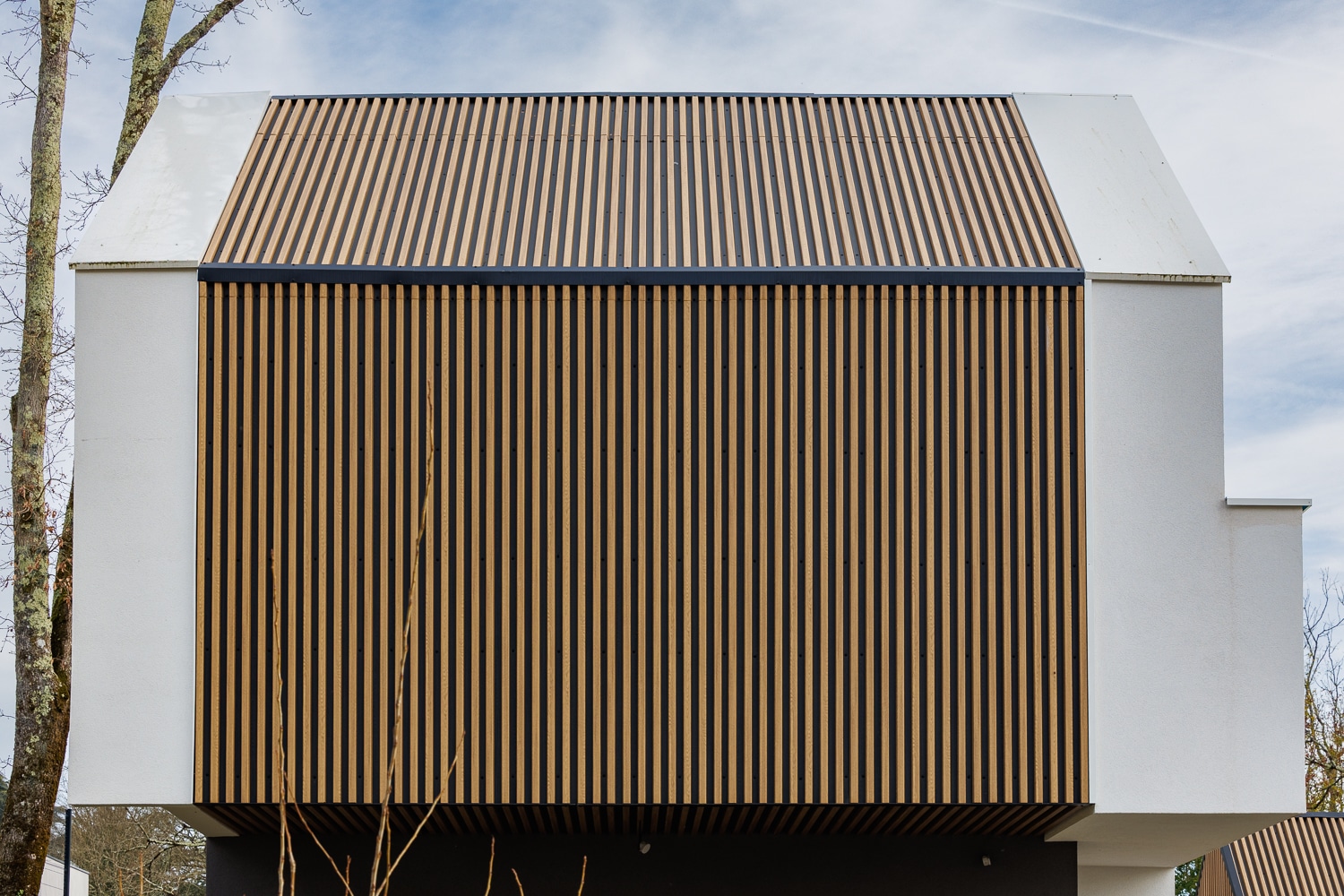 Façade moderne en bois à claire-voie et murs blancs d'une maison contemporaine sous un ciel nuageux.