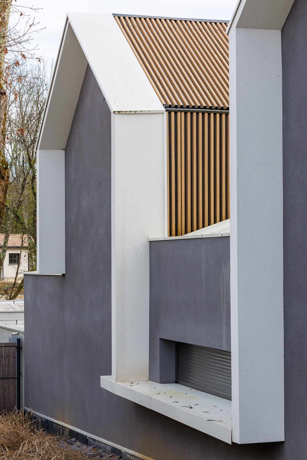 Détail architectural d'une maison moderne : murs gris, cadres blancs saillants et bardage en bois vertical.