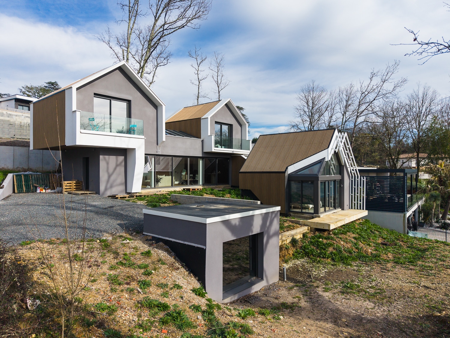 Maison d'architecte moderne avec toits à pignons, bardage bois et grandes baies vitrées sur terrain en pente.