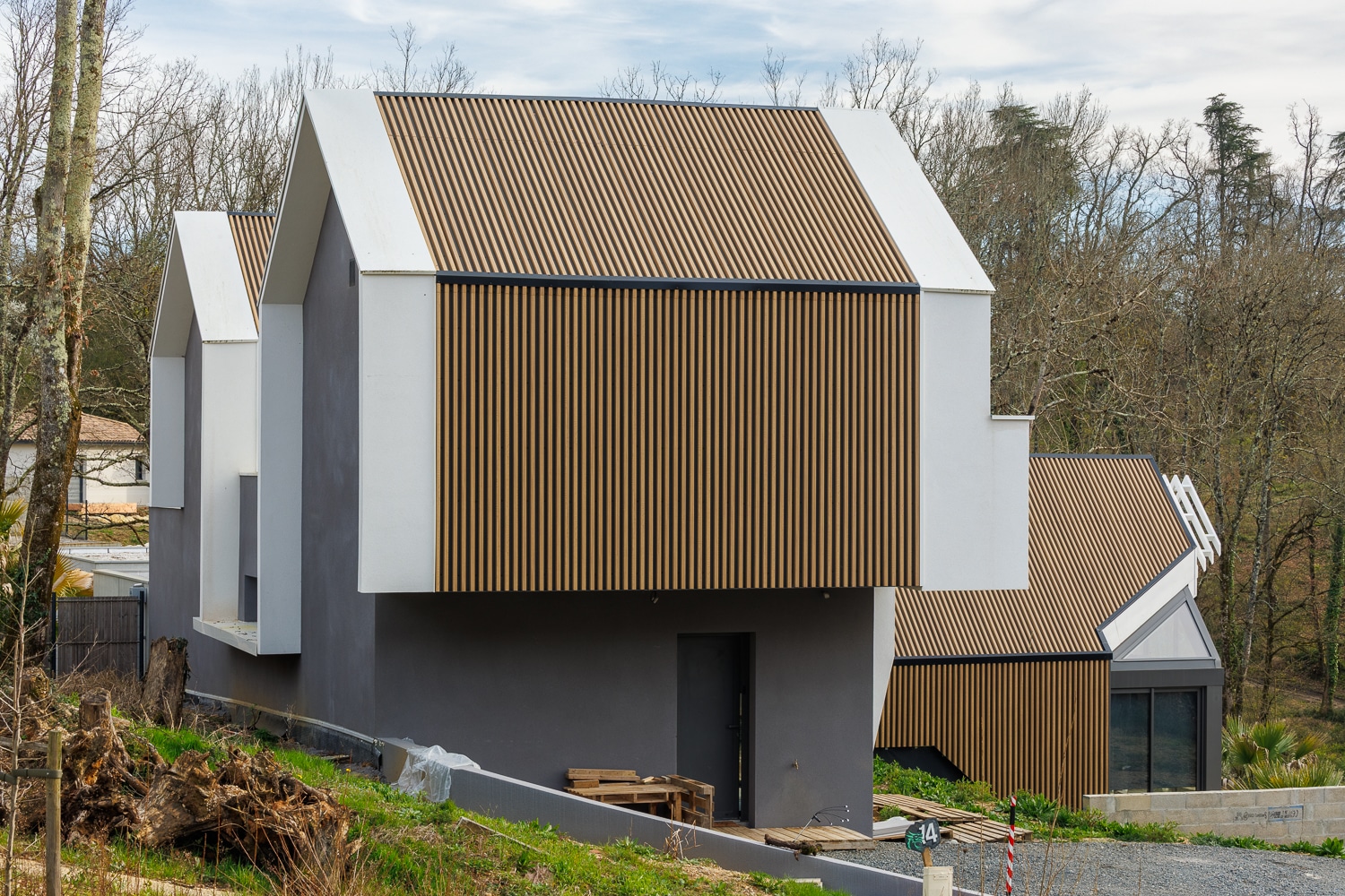 Maison contemporaine à l'architecture minimaliste avec bardage bois vertical et murs gris en lisière de forêt.