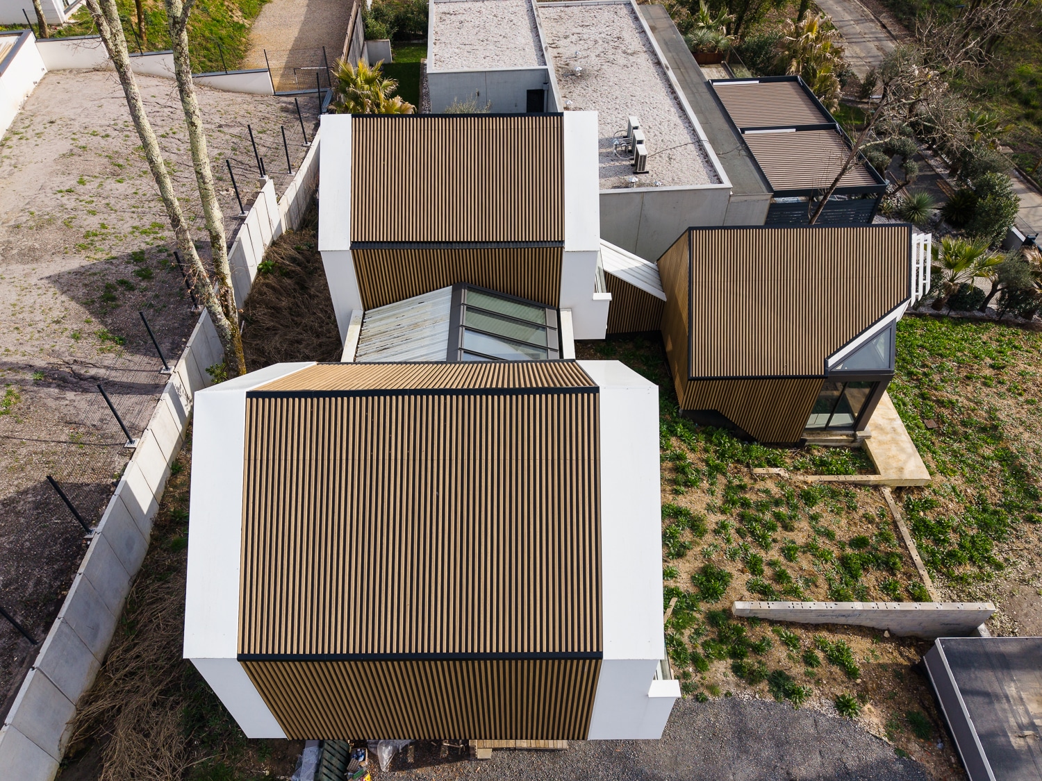 Maison contemporaine à l'architecture géométrique en lattes de bois et façades blanches vue du dessus.