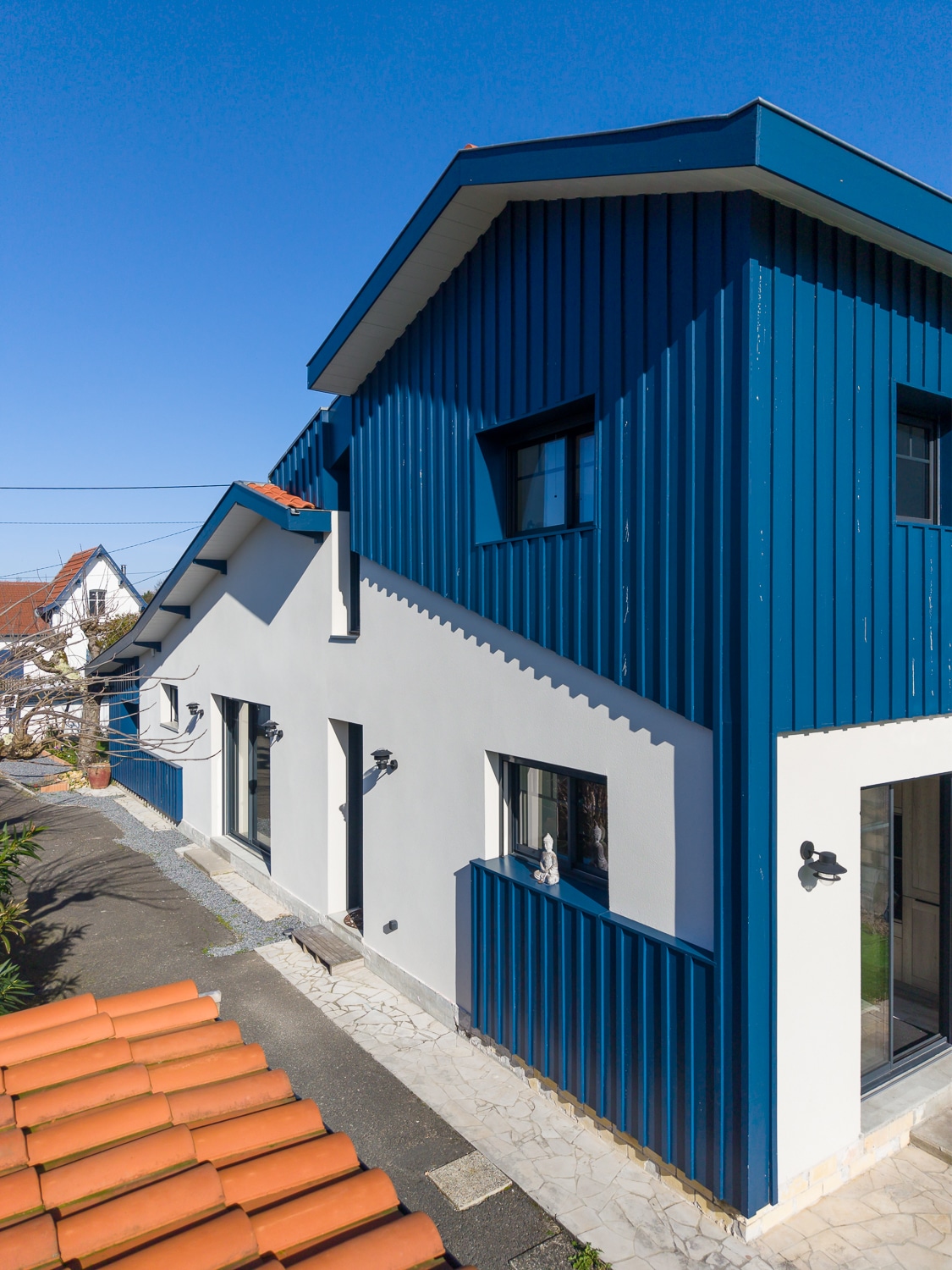 Maison contemporaine à façade bicolore blanche et bardage bleu avec toit en tuiles terre cuite.