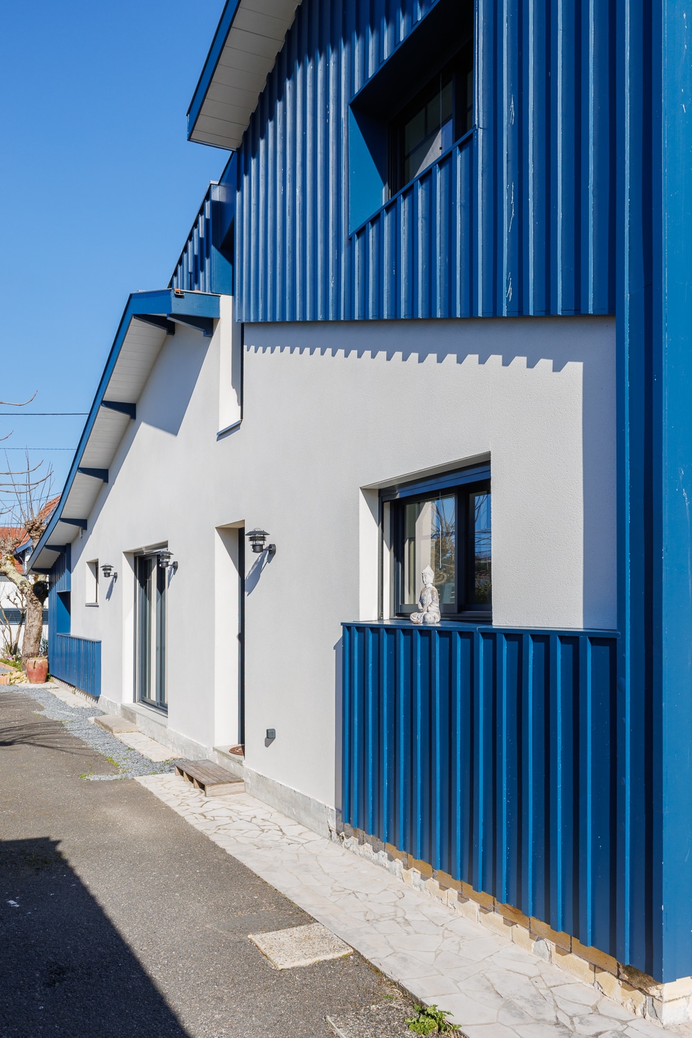 Maison moderne avec façade blanche et bardage vertical bleu intense sous un ciel dégagé.