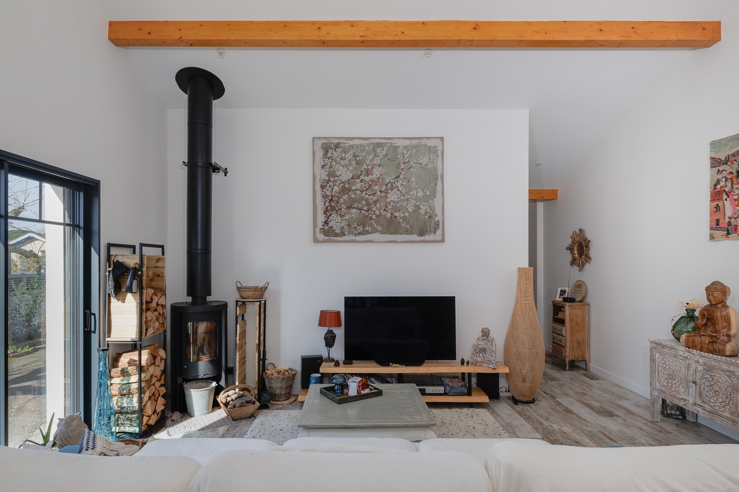 Salon moderne et chaleureux avec poêle à bois noir, grand tableau fleuri et poutre en bois apparente.